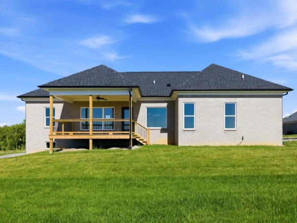 Modern brick home with a wooden porch and green lawn under a blue sky.