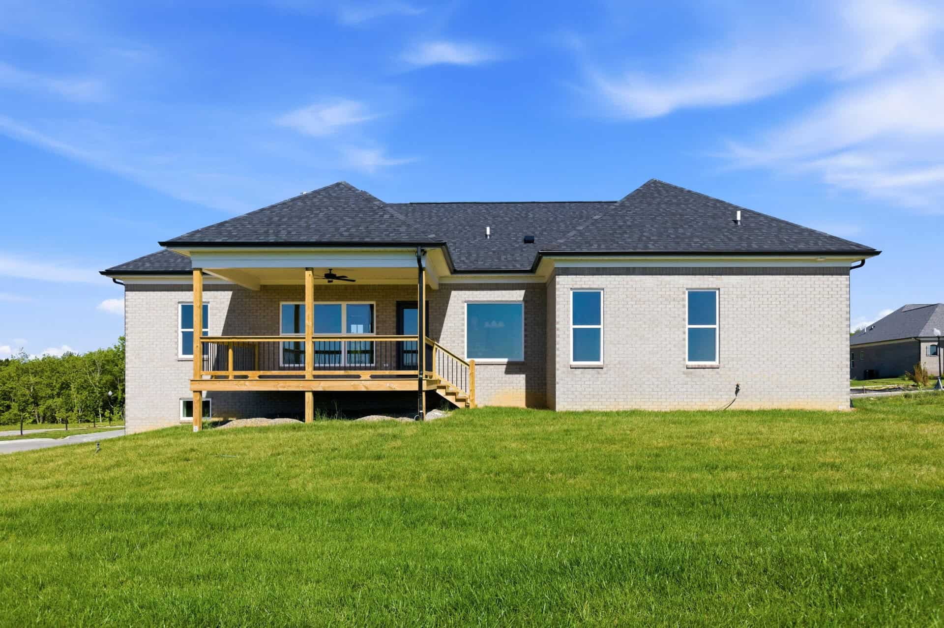Modern brick home with a wooden porch and green lawn under a blue sky.