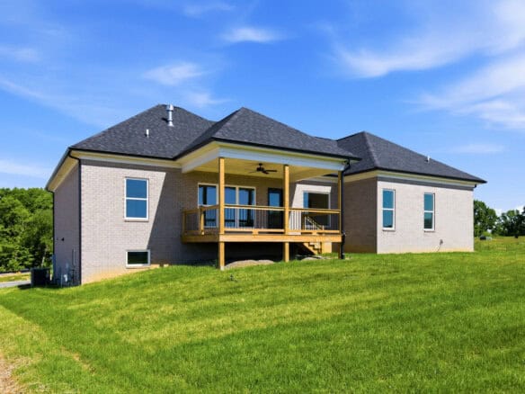 Two-story brick house with a wooden deck and stairs, set on a green lawn under a clear blue sky.