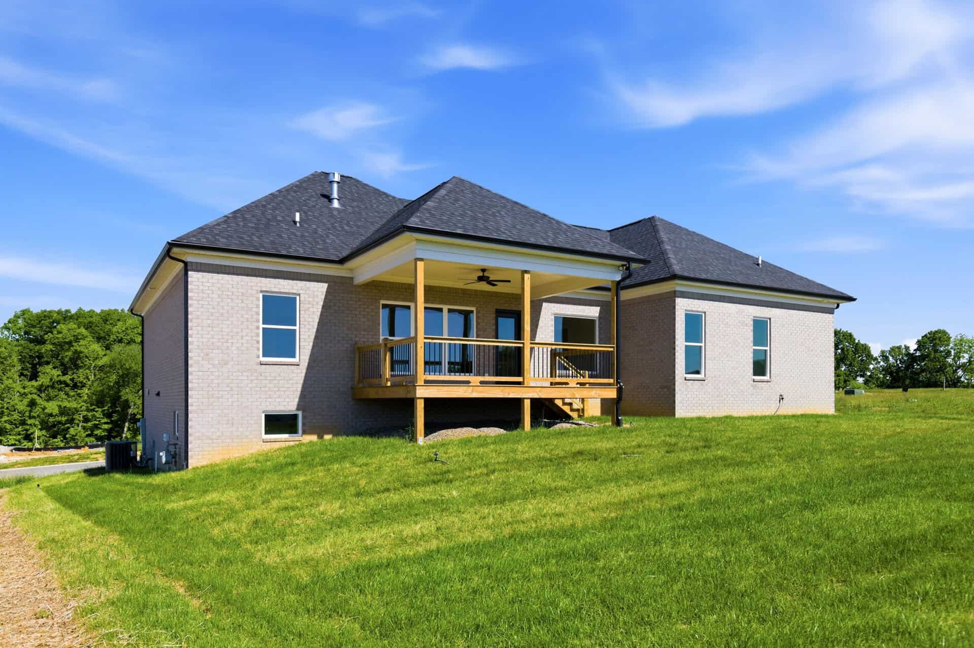 Two-story brick house with a wooden deck and stairs, set on a green lawn under a clear blue sky.