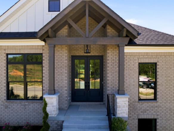Brick house entrance with dark double doors under a covered porch and wooden beams.