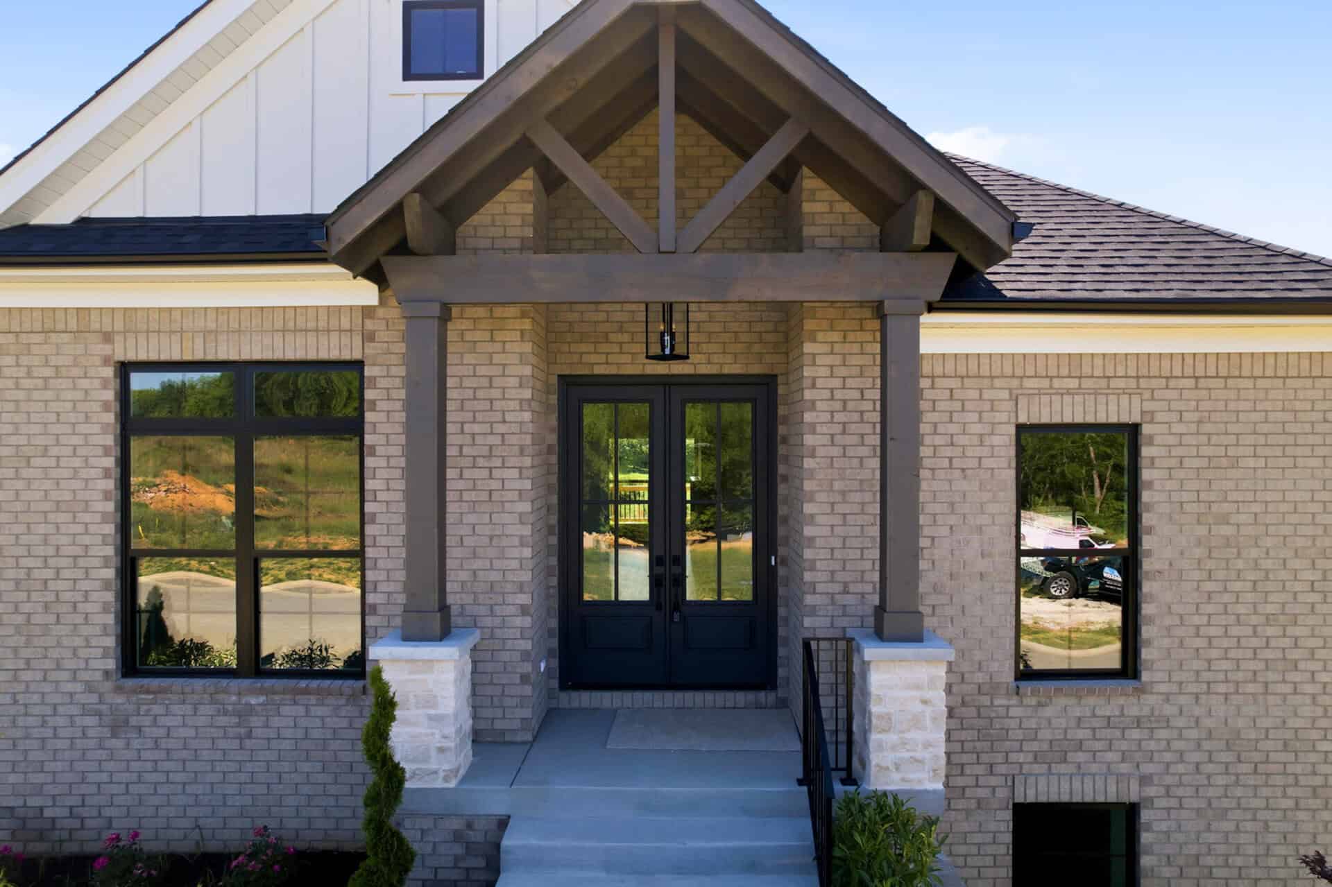Brick house entrance with dark double doors under a covered porch and wooden beams.