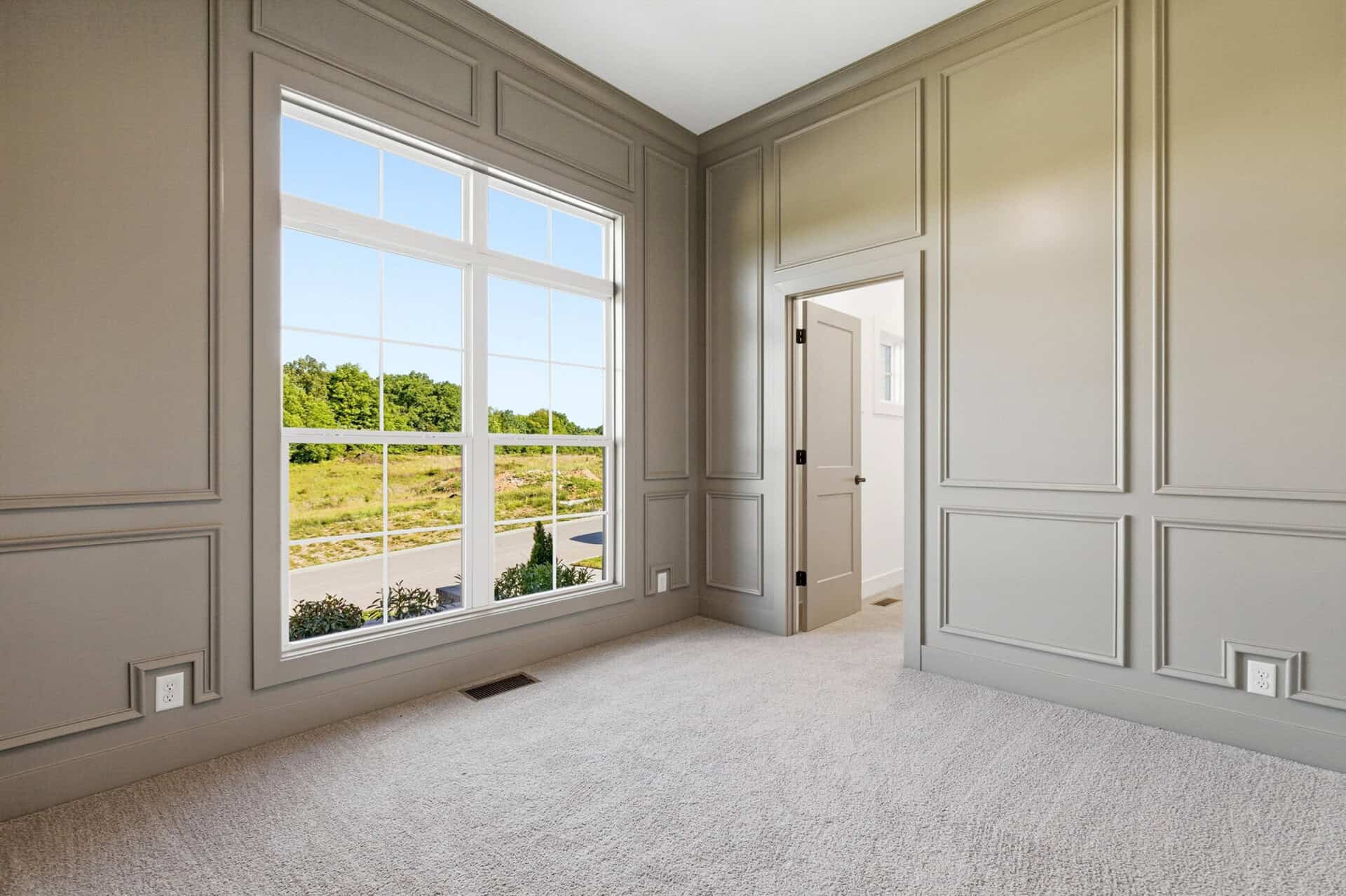 Bright room with large window and neutral wall paneling in a luxury home.