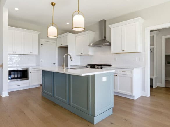 Bright modern kitchen with white cabinets, light countertops, and a blue-gray island under gold pendant lights.