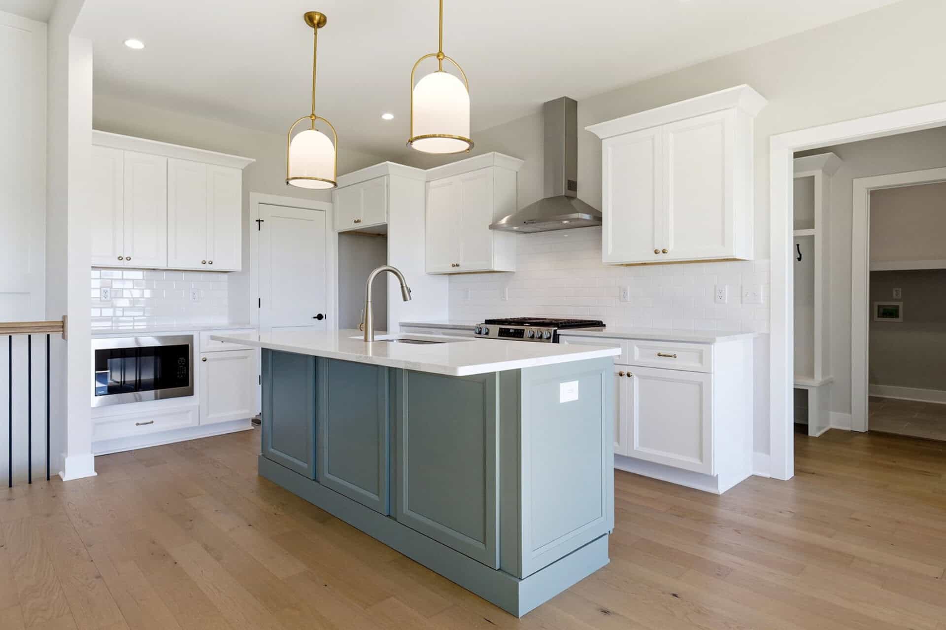 Bright modern kitchen with white cabinets, light countertops, and a blue-gray island under gold pendant lights.
