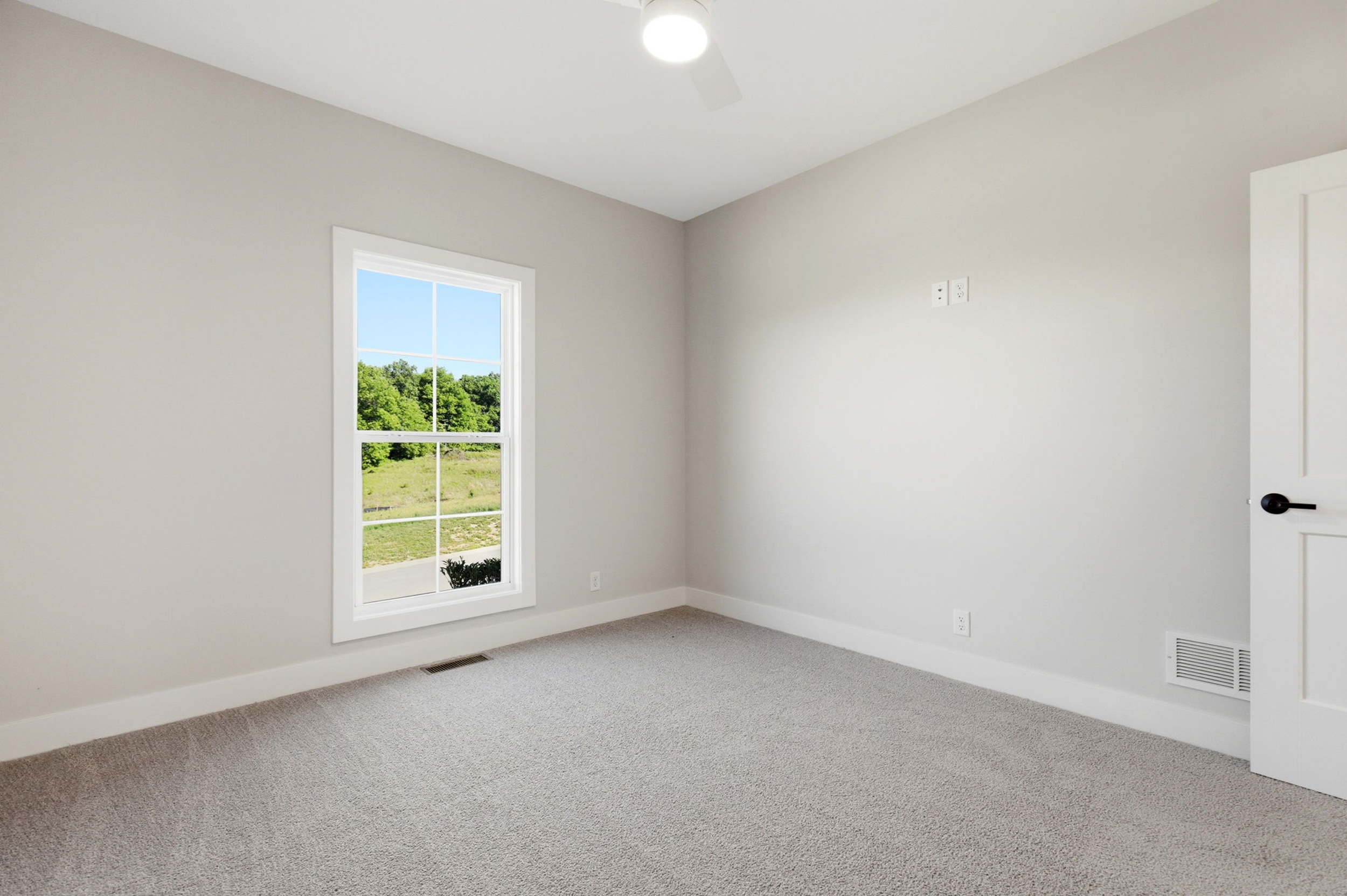 Empty room with a window overlooking green landscape and a white door.