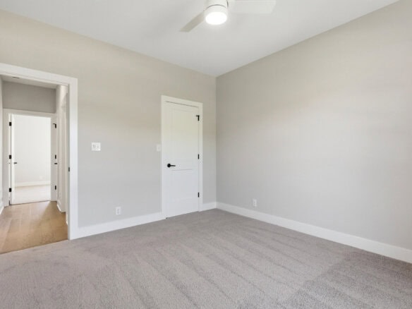Empty gray-walled bedroom with white doors, light carpet, and a ceiling fan