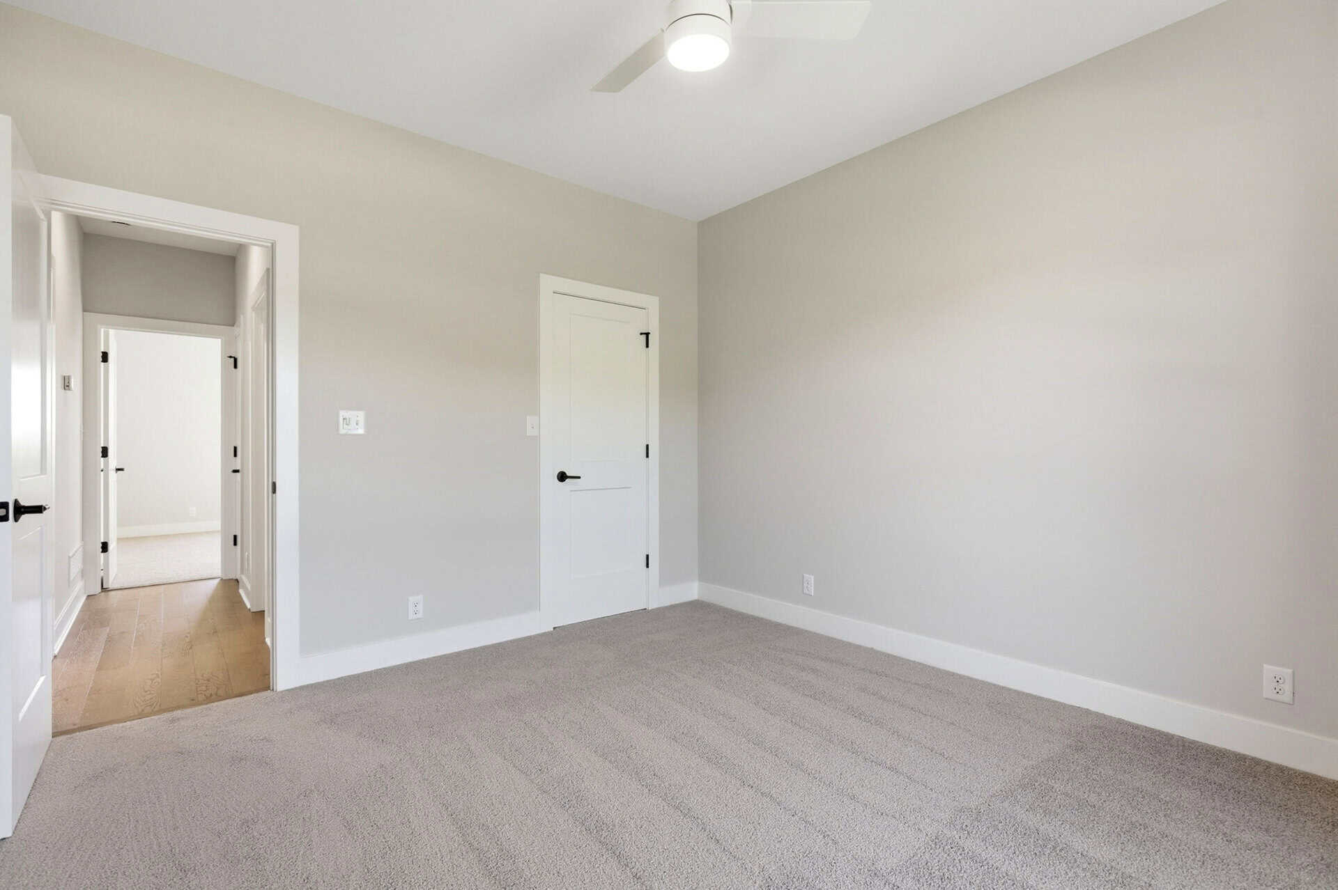 Empty gray-walled bedroom with white doors, light carpet, and a ceiling fan
