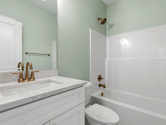 White bathroom vanity with marble countertop and gold faucet, next to a white toilet in a mint-green bathroom.