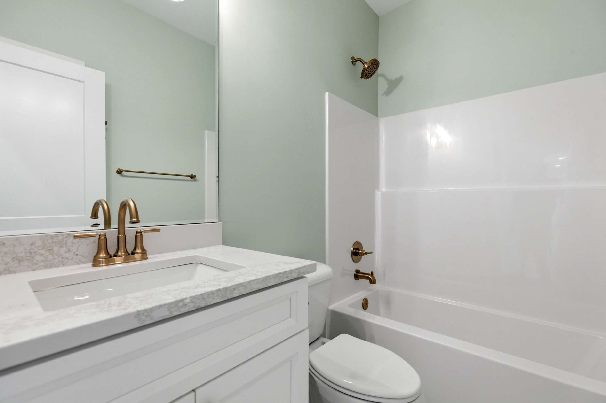 White bathroom vanity with marble countertop and gold faucet, next to a white toilet in a mint-green bathroom.