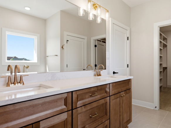 Modern bathroom with a wood vanity, white marble countertop, and gold-finished faucets beneath a large mirror and warm lighting.