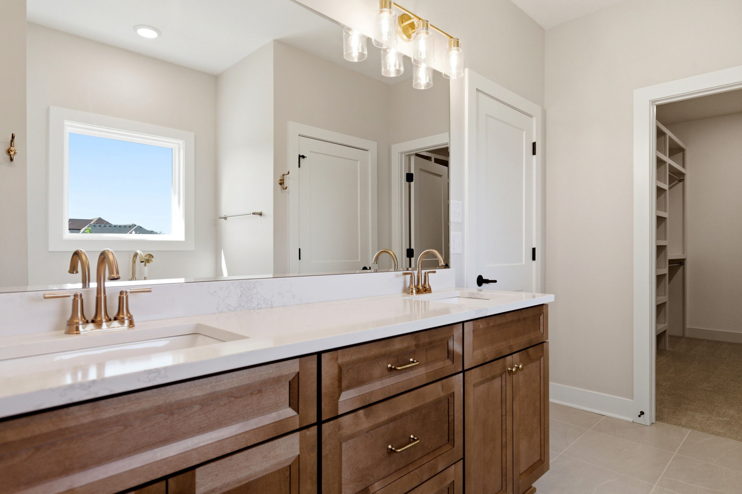 Modern bathroom with a wood vanity, white marble countertop, and gold-finished faucets beneath a large mirror and warm lighting.