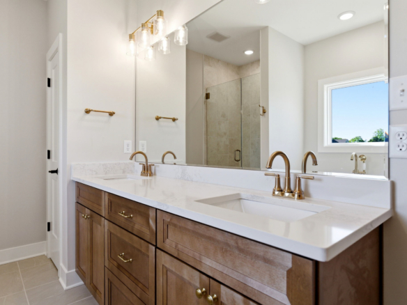 Double-sink bathroom vanity with wood cabinets, marble countertop, brass faucets, and large mirror.