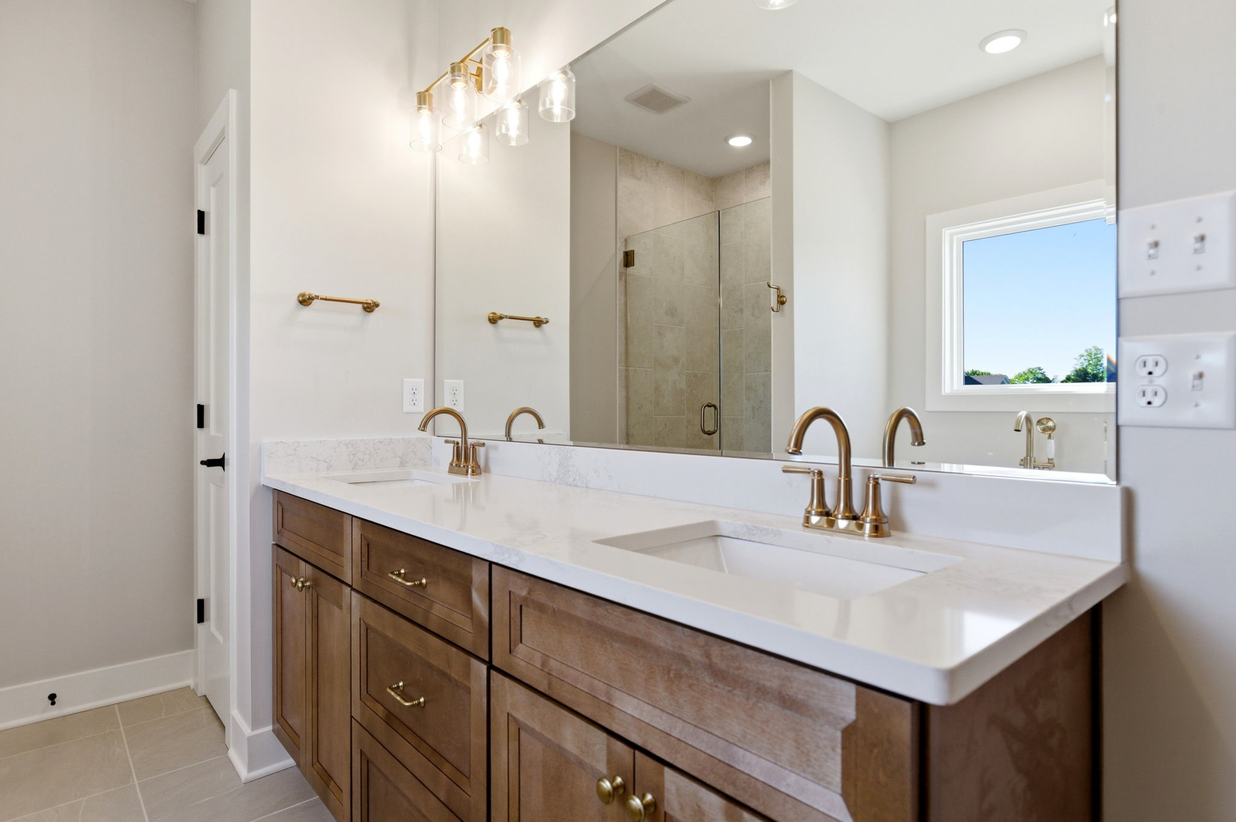 Double-sink bathroom vanity with wood cabinets, marble countertop, brass faucets, and large mirror.