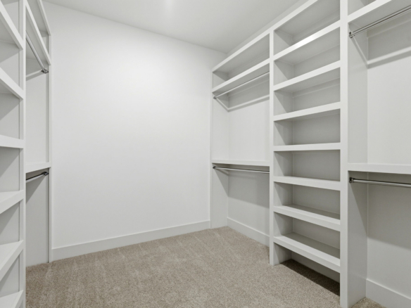 White walk-in closet with built-in shelving and hanging rods on both sides, carpeted floor, empty shelves ready for storage.