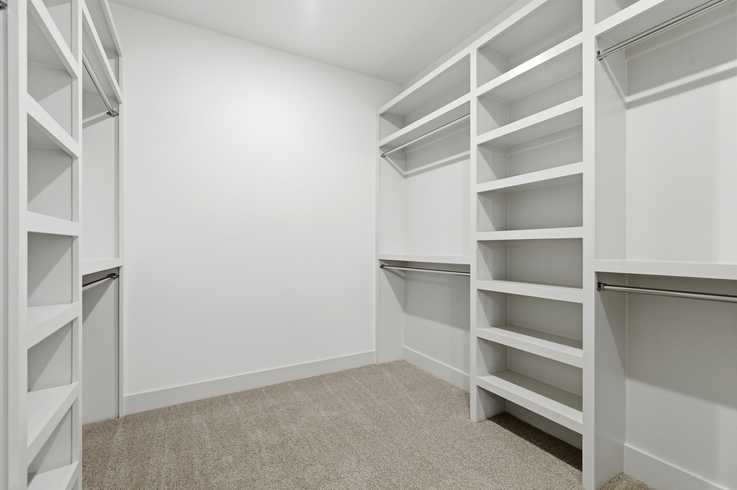 White walk-in closet with built-in shelving and hanging rods on both sides, carpeted floor, empty shelves ready for storage.