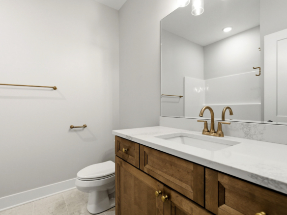 Modern bathroom with white walls, gold fixtures, and a wooden vanity with a marble countertop and sink.