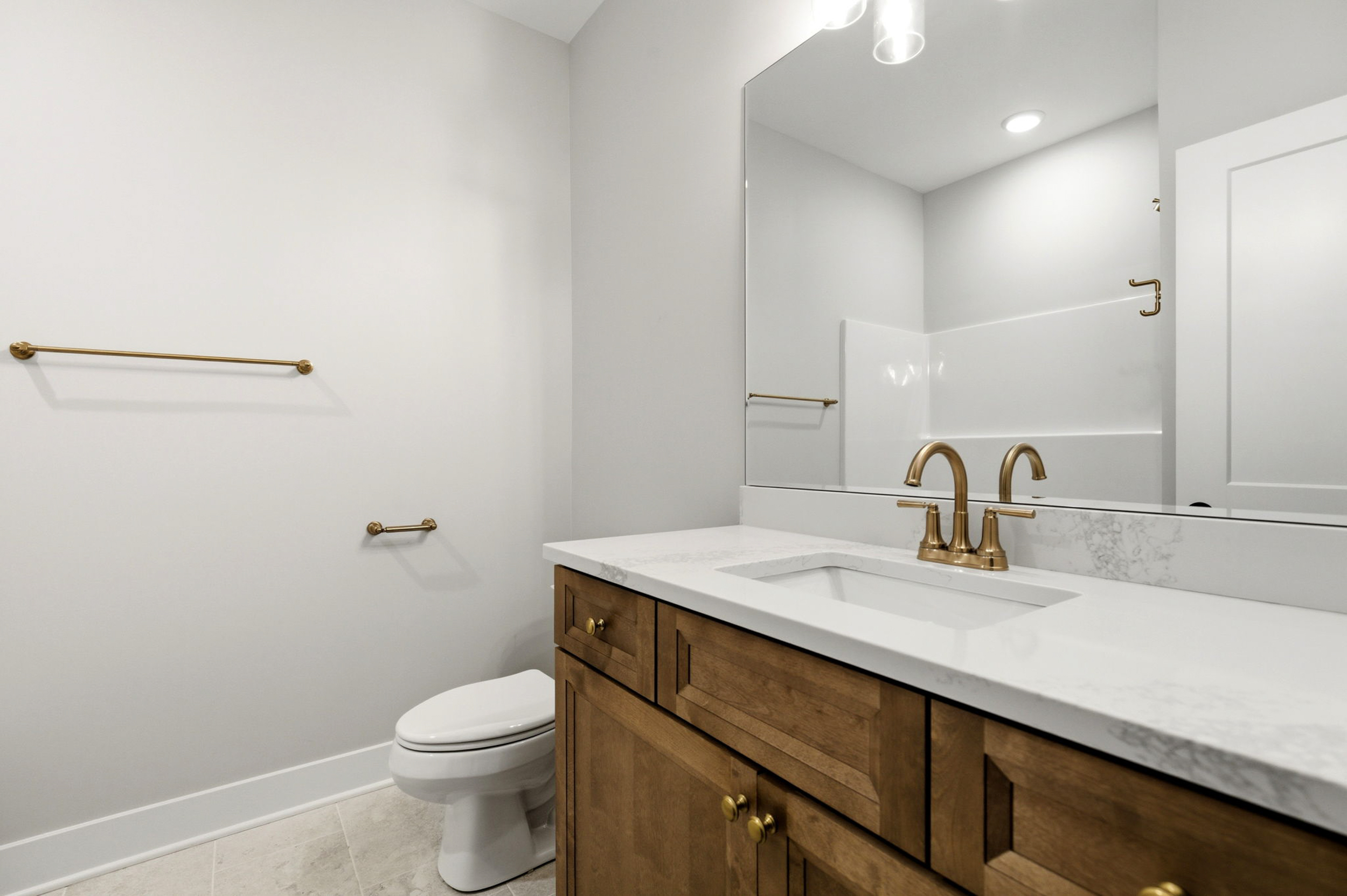 Modern bathroom with white walls, gold fixtures, and a wooden vanity with a marble countertop and sink.