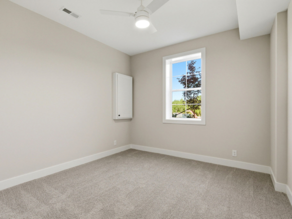 Unfurnished beige room with white baseboards, a window showing trees outside, and a ceiling fan to the center of the ceiling.