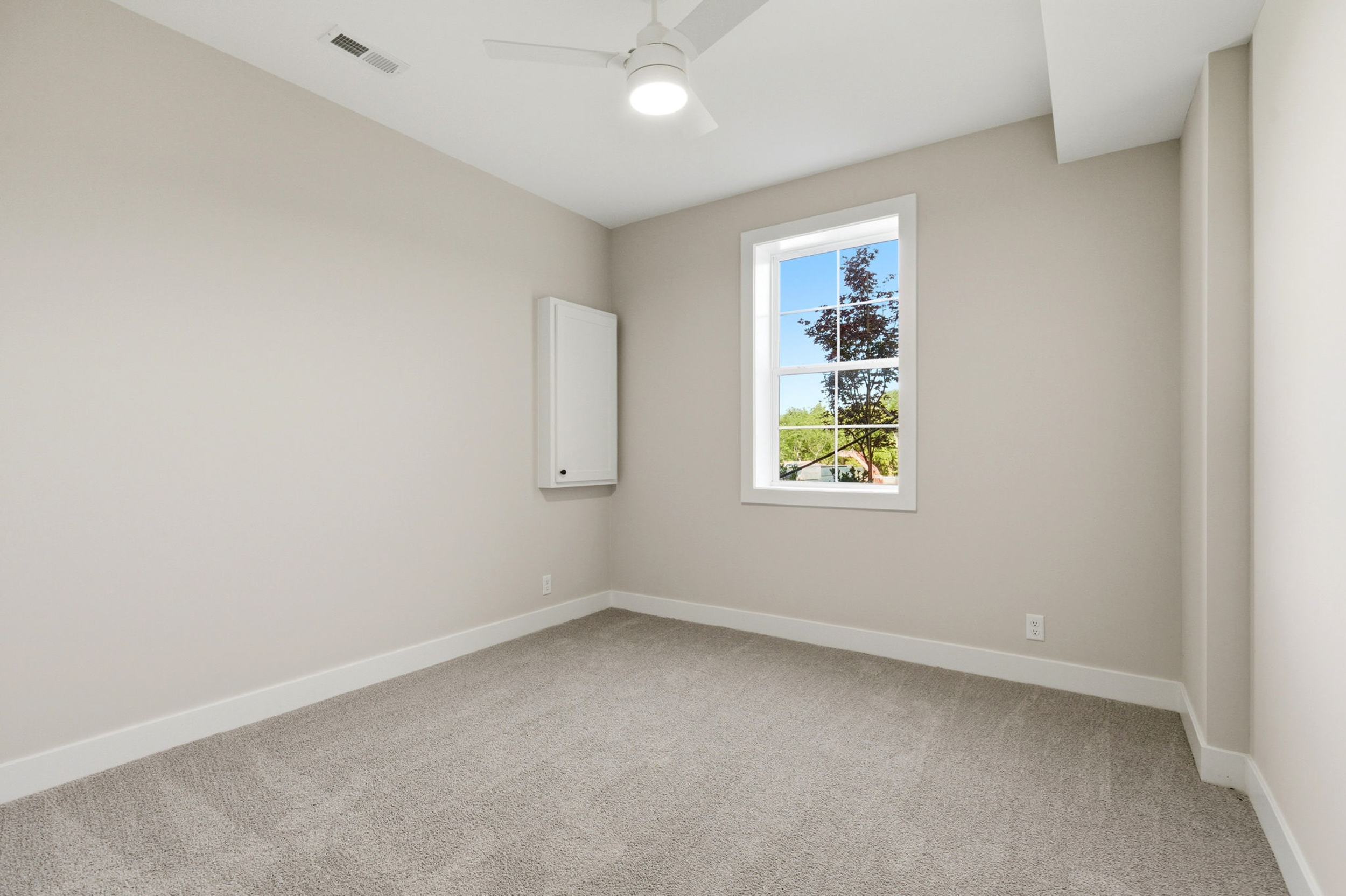 Unfurnished beige room with white baseboards, a window showing trees outside, and a ceiling fan to the center of the ceiling.