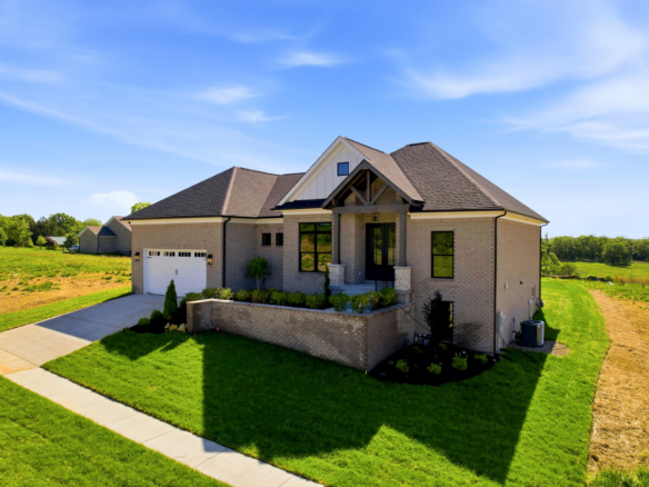 Front view of a modern brick house with a two-car garage, a paved driveway, and a green lawn under a clear blue sky.
