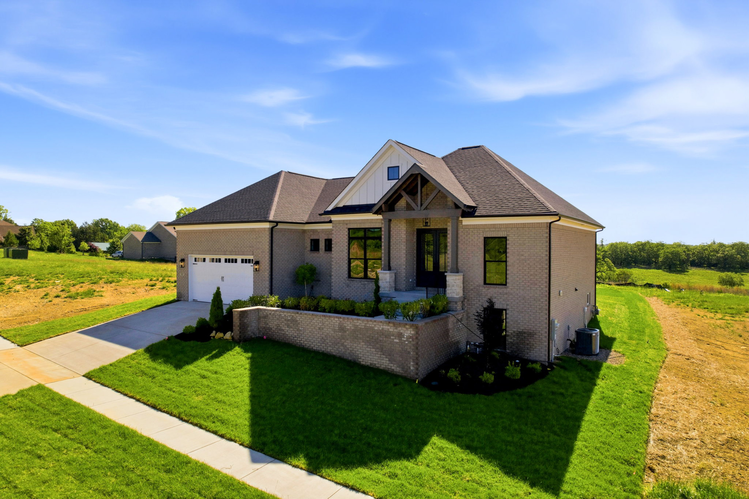 Photography by AS Media Co Front view of a modern brick house with a two-car garage, a paved driveway, and a green lawn under a clear blue sky.