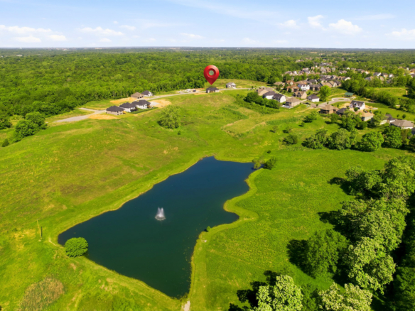 Aerial view of a suburban neighborhood around a pond with a fountain; a red map pin marks a central house area.