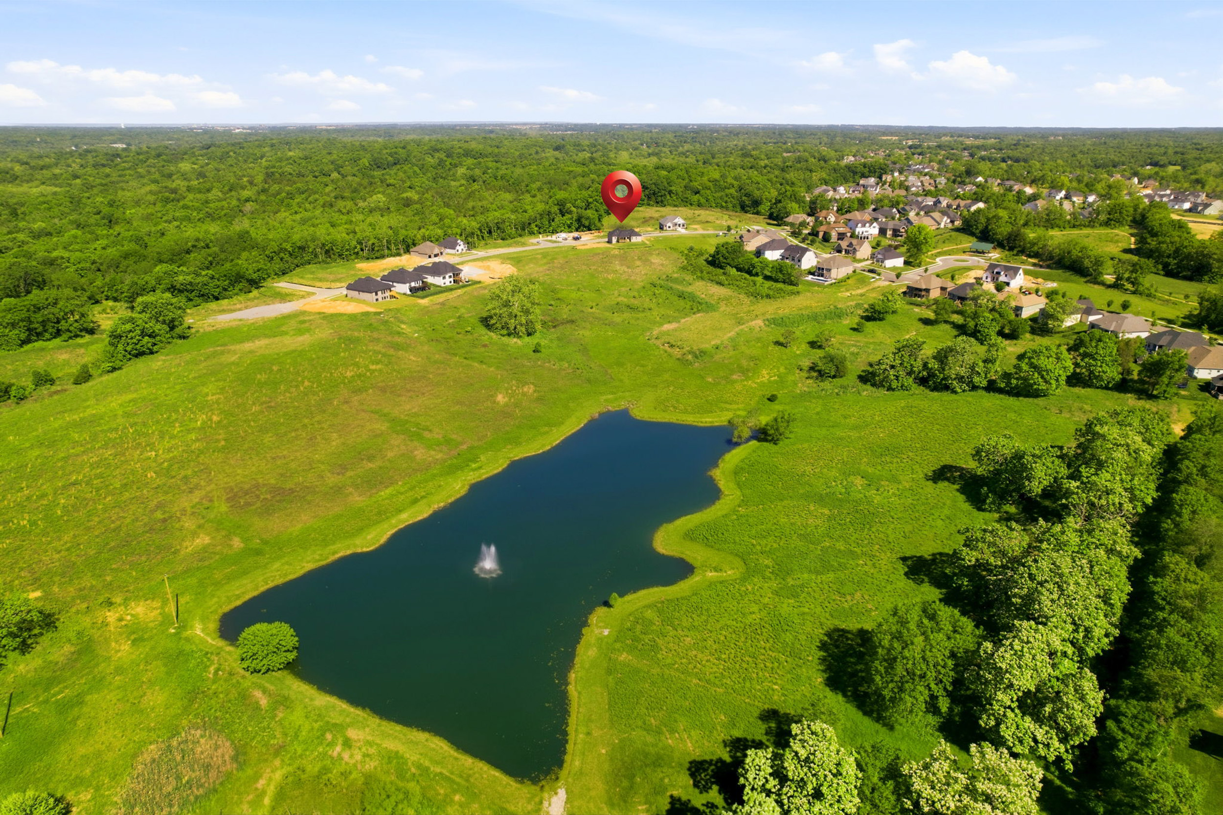 Aerial view of a suburban neighborhood around a pond with a fountain; a red map pin marks a central house area.