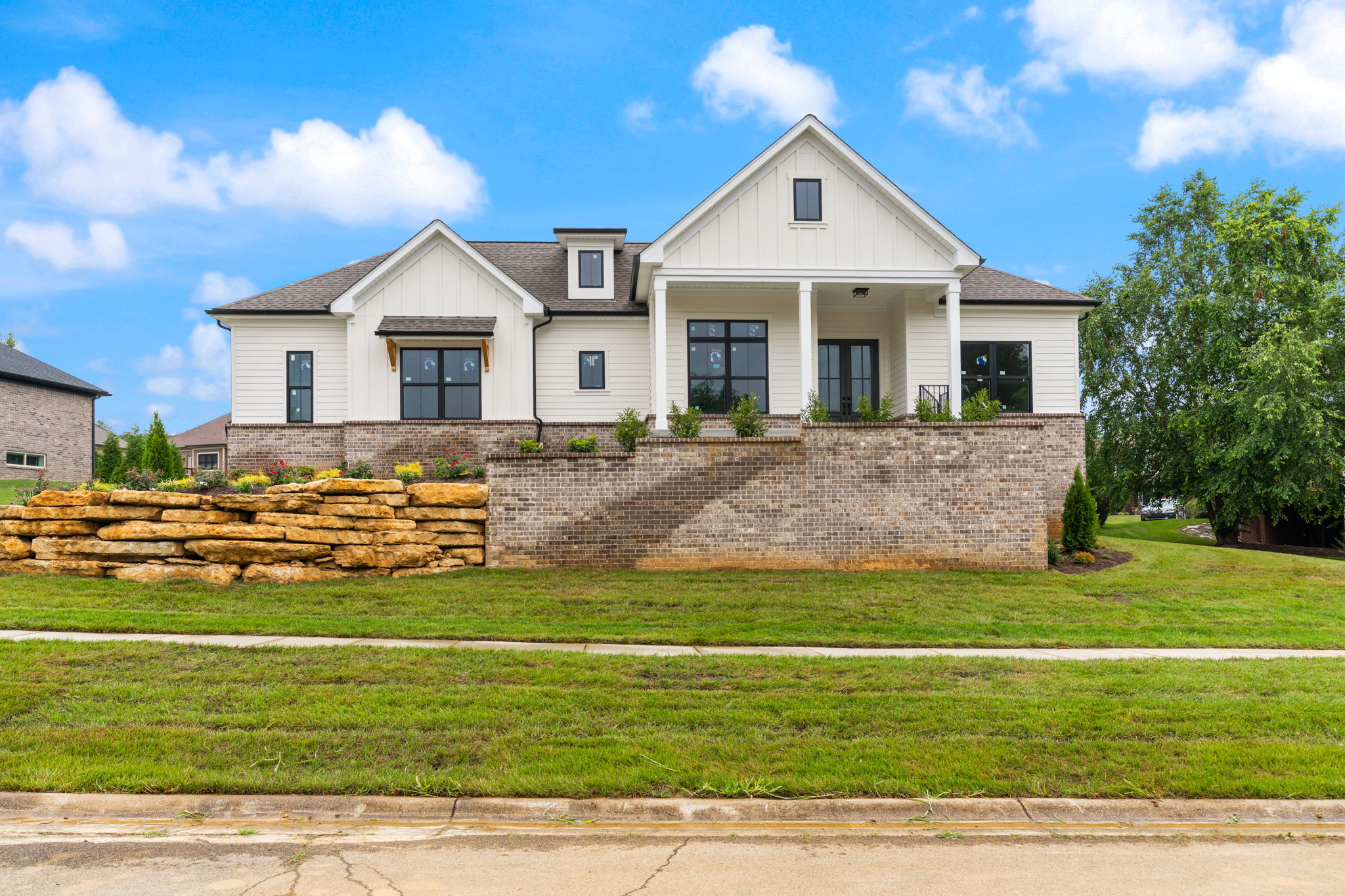 Front view of a modern white siding house with brick foundation and a stone retaining wall under a bright blue sky.