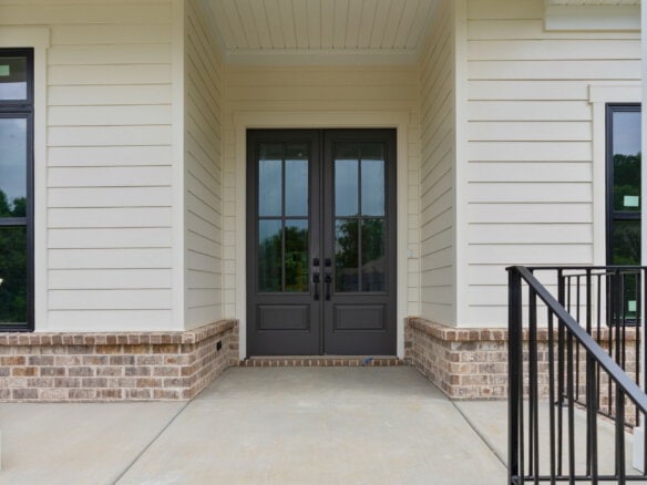 Front entrance with black double doors and brick foundation in a modern home.