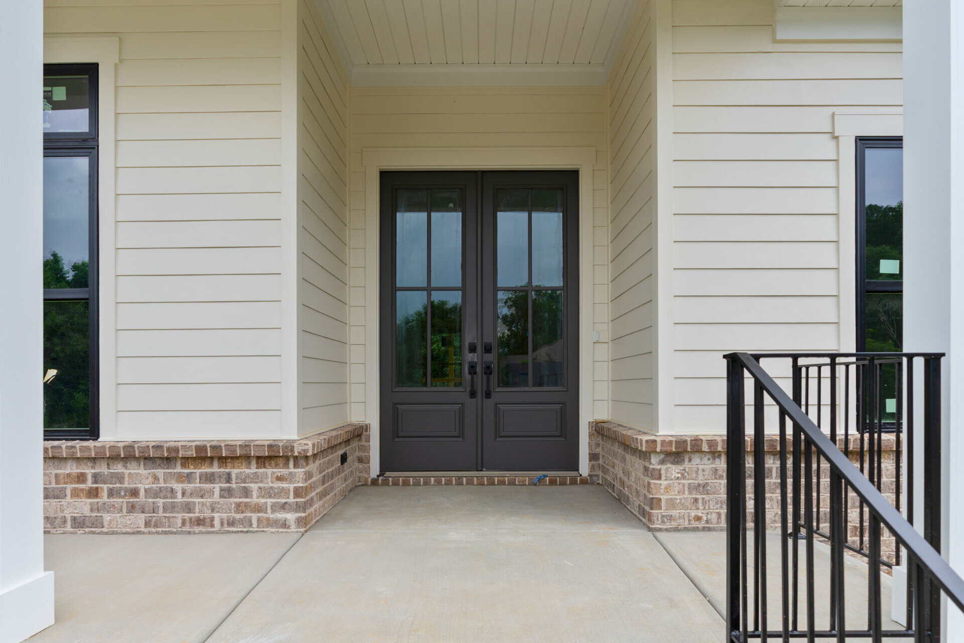 Front entrance with black double doors and brick foundation in a modern home.