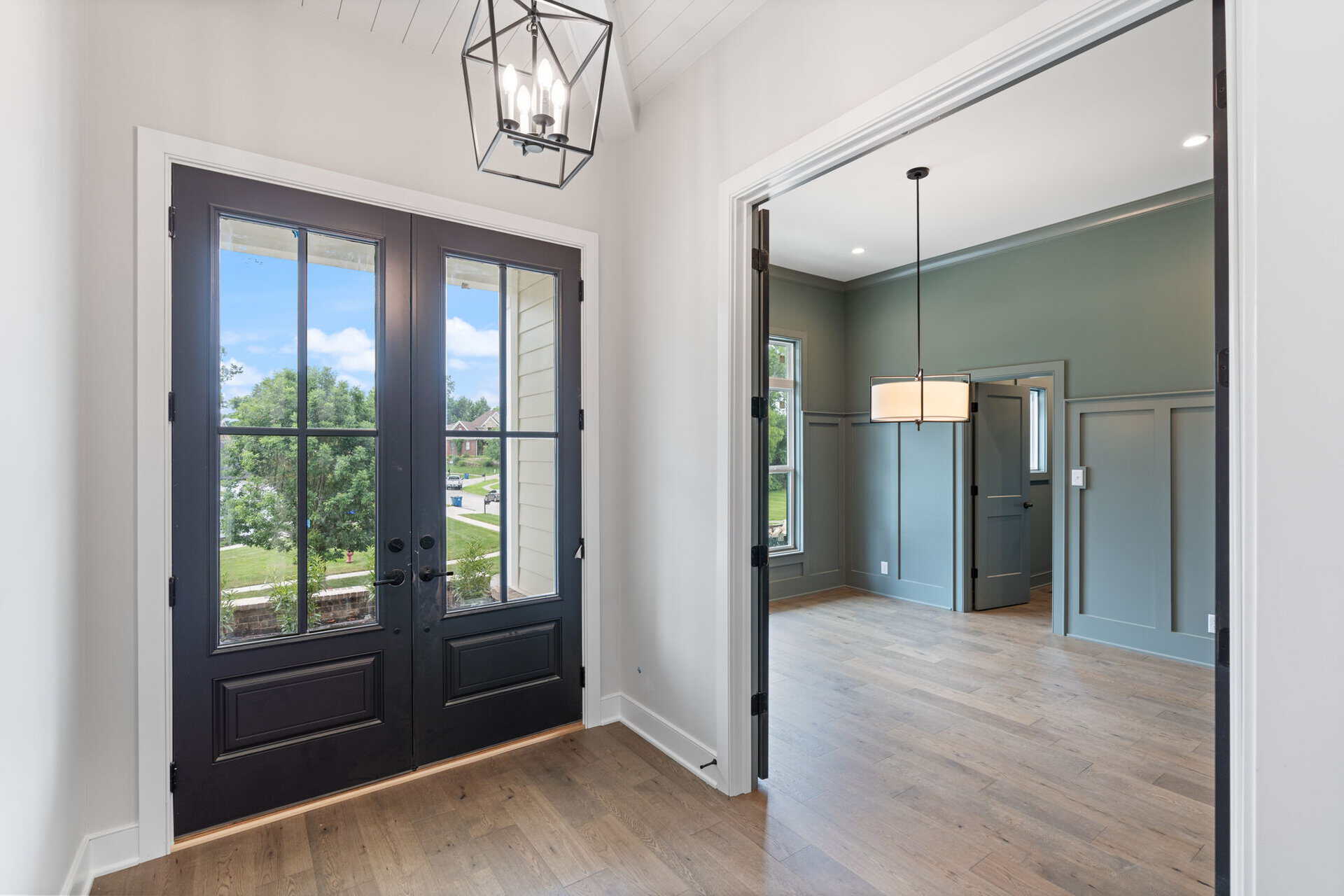 Elegant entryway with black door and view into living room with green walls.