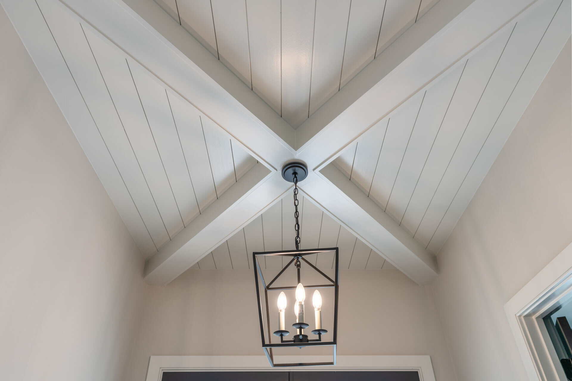 Interior ceiling with white wood paneling and a black chandelier.