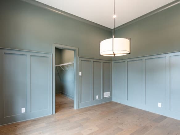 Empty room with blue-green walls, wooden floor, and modern ceiling light fixture.