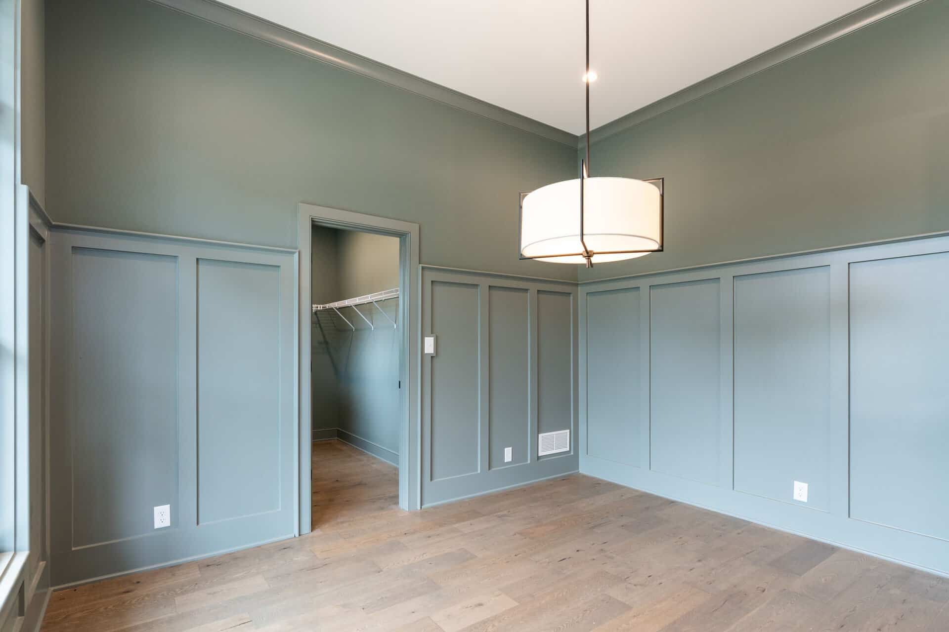 Empty room with blue-green walls, wooden floor, and modern ceiling light fixture.