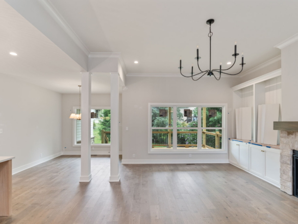 Open-concept living space with gray walls, white trim, a black multi-arm chandelier, large windows, and a fireplace with white cabinets beside.