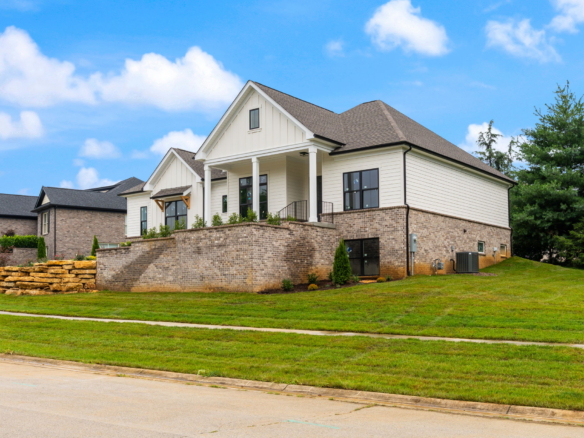 Front view of a two-story suburban house with brick first level, white siding, and a manicured lawn under a blue sky with clouds.