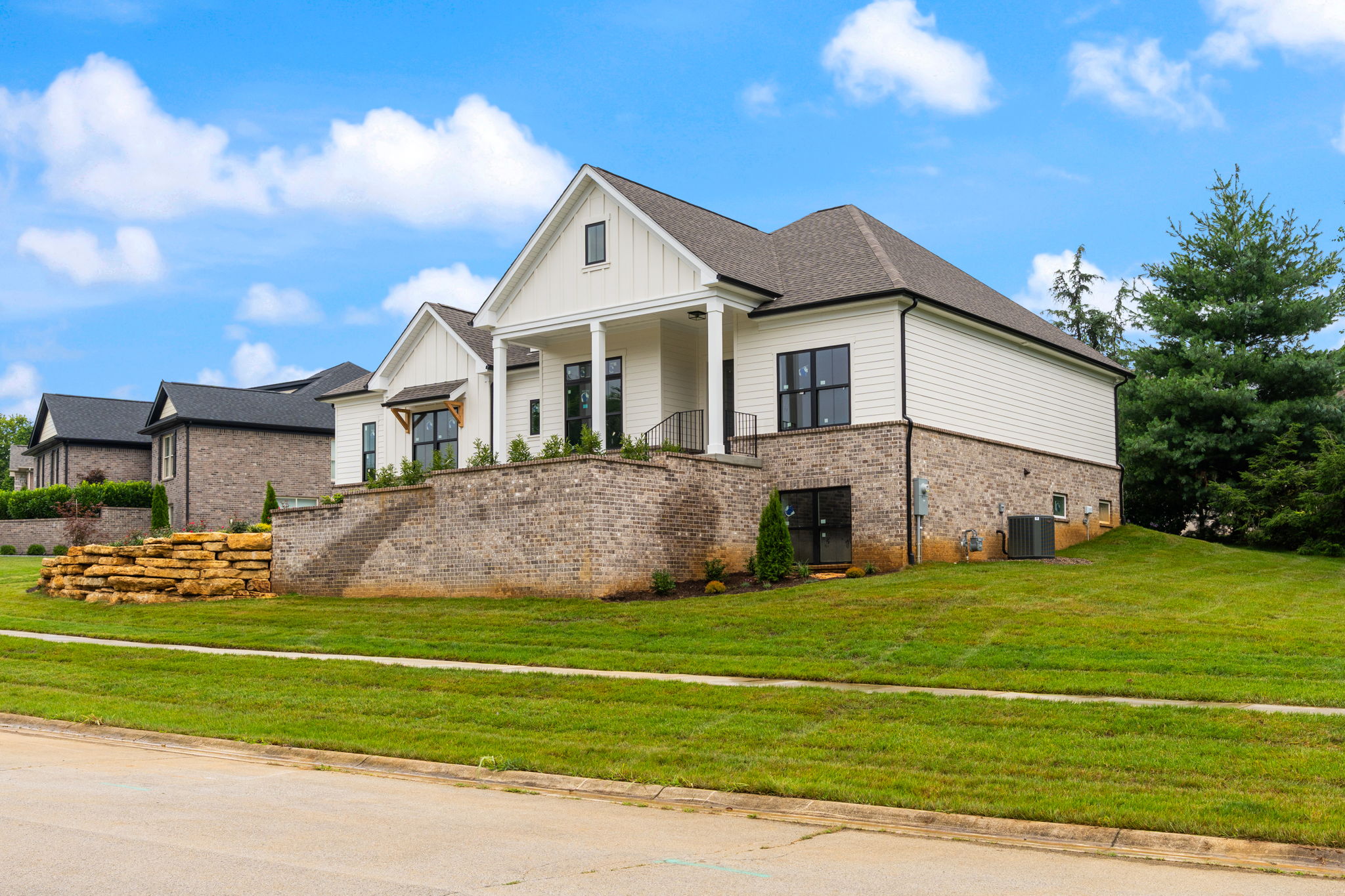 Front view of a two-story suburban house with brick first level, white siding, and a manicured lawn under a blue sky with clouds.