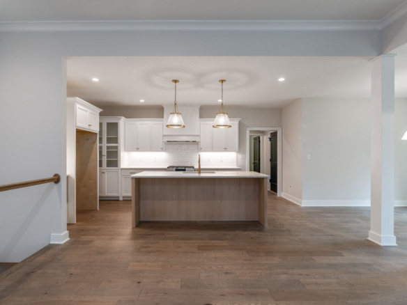 Open kitchen with white cabinets, a wooden island, and two brass pendant lights.