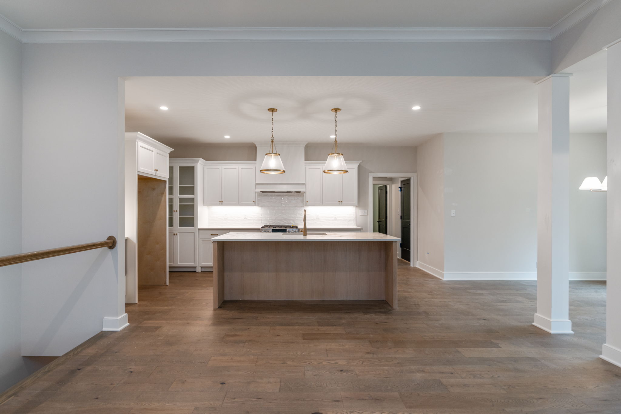 Open kitchen with white cabinets, a wooden island, and two brass pendant lights.