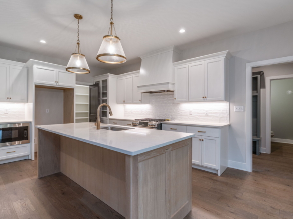 Bright, modern kitchen with white cabinets, marble island, and two brass pendant lights over the counter.