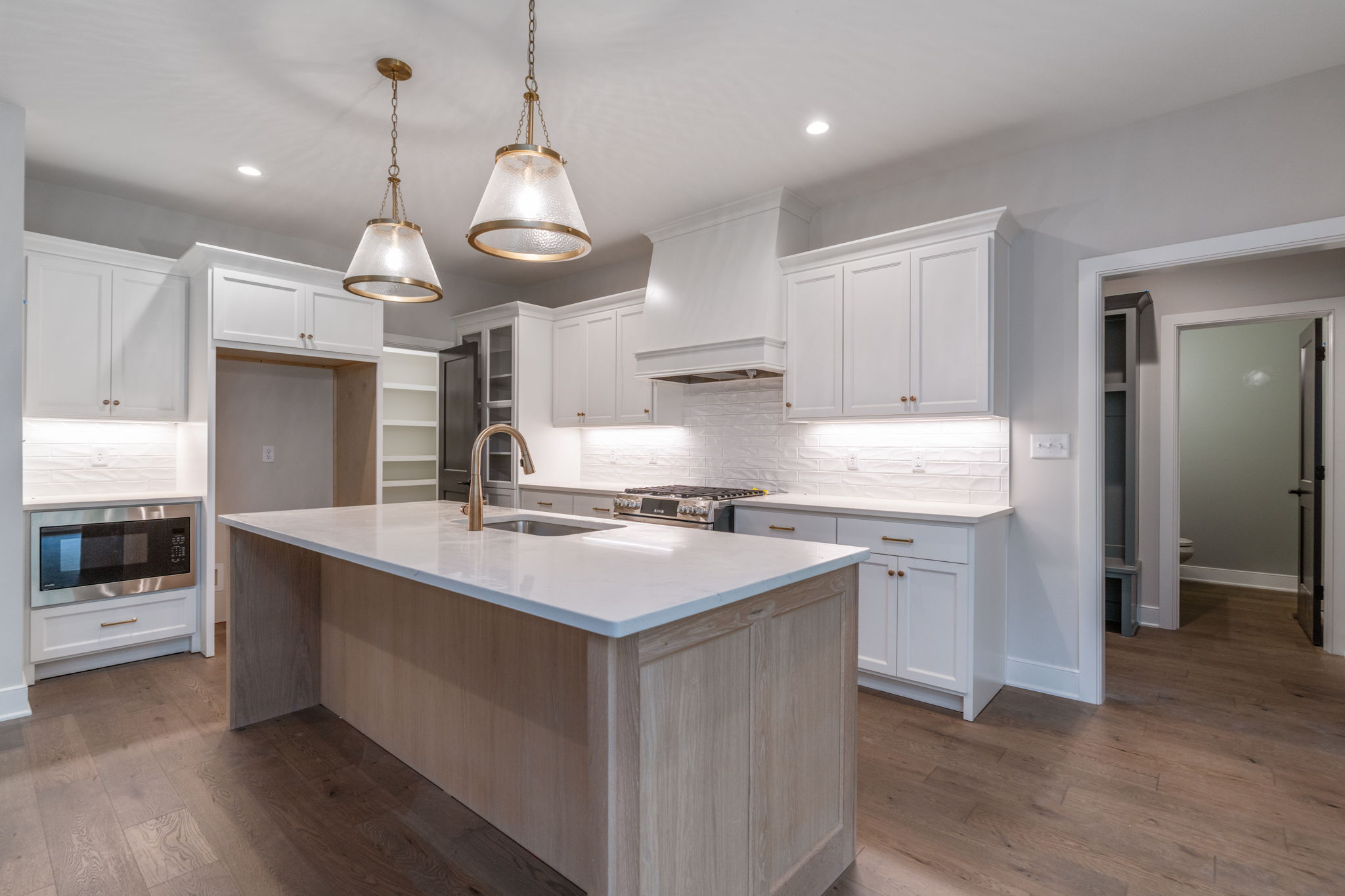 Bright, modern kitchen with white cabinets, marble island, and two brass pendant lights over the counter.