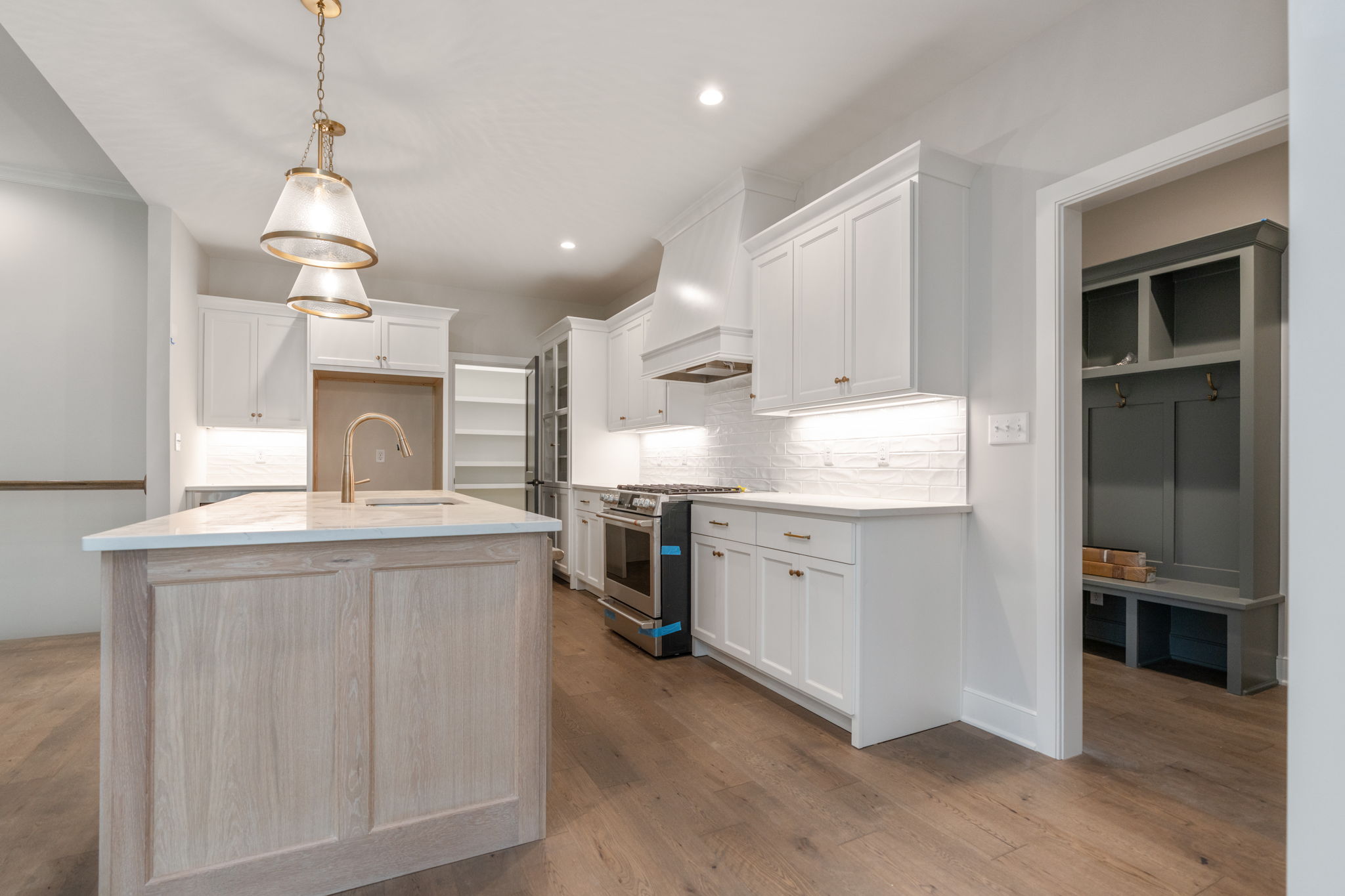 Modern white-kitchen with an island, pendant lights, and stainless steel appliances; warm wood floors.
