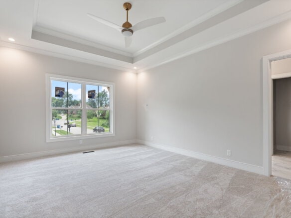 Bright empty bedroom with large window and tray ceiling in new home.