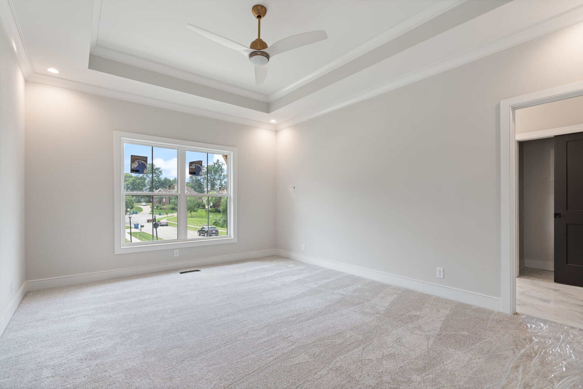 Bright empty bedroom with large window and tray ceiling in new home.