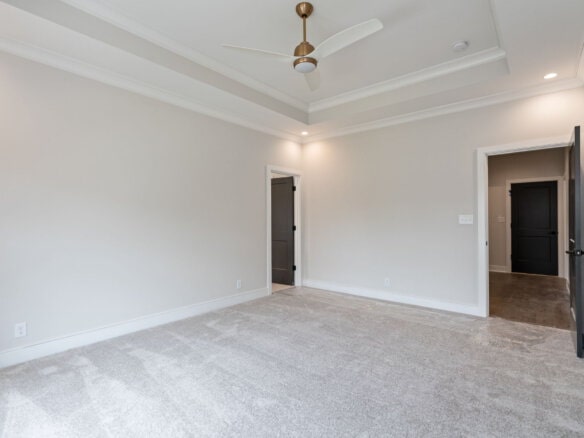Empty modern living room with white walls, ceiling fan, and beige carpet.