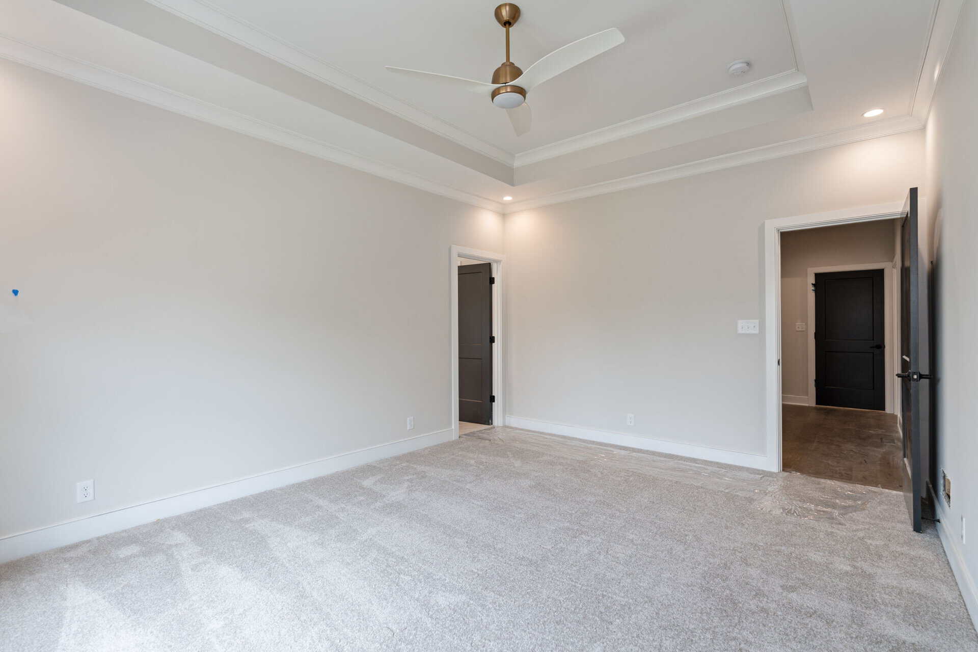 Empty modern living room with white walls, ceiling fan, and beige carpet.
