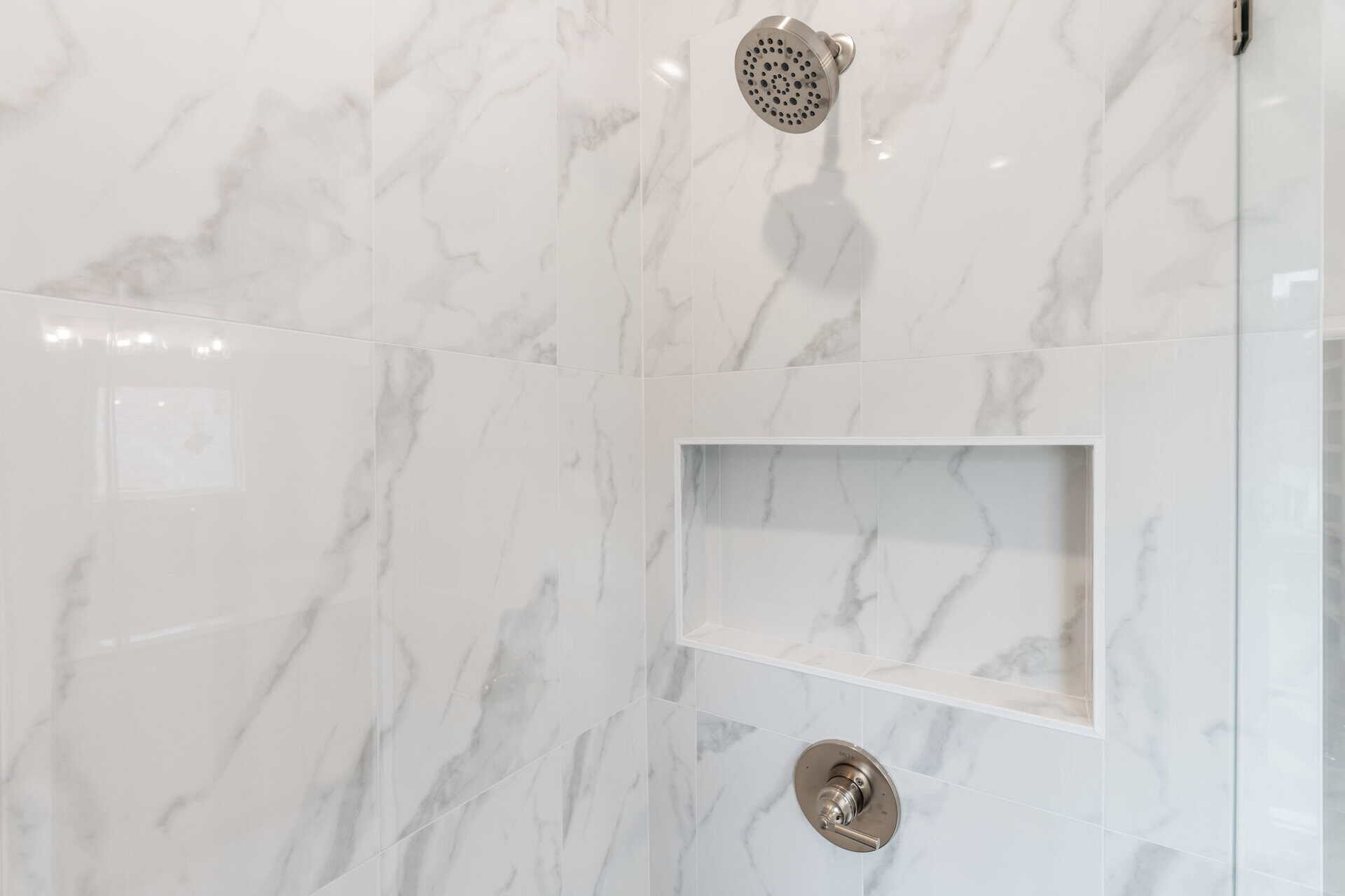 Close-up of a modern shower with marble tiles and built-in niche.