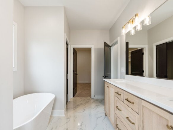 Modern bathroom with white bathtub, double vanity, and marble floors.