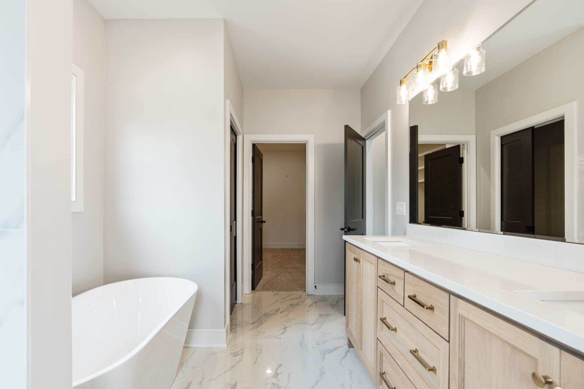 Modern bathroom with white bathtub, double vanity, and marble floors.